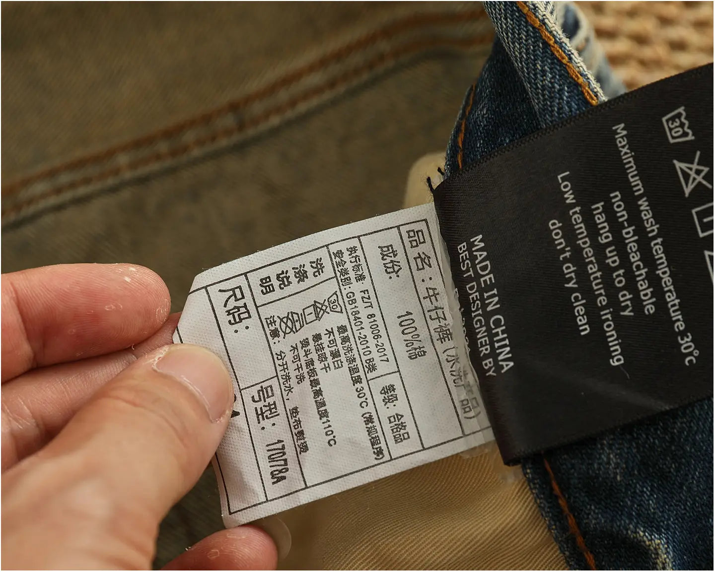Black and white garment care label attached to the back side of distressed patchwork denim jeans men in blue denim.