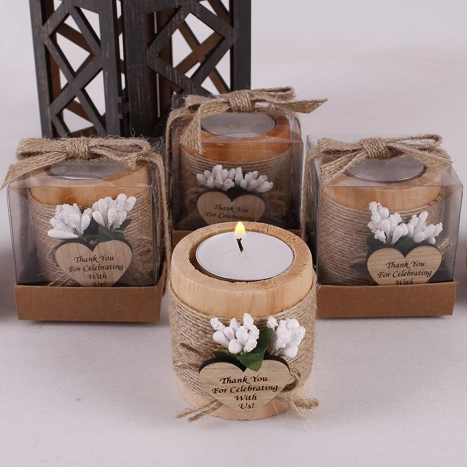 Un bougeoir rustique en bois pour petite bougie chauffe-plat, enveloppé d’une cordelette naturelle, avec une touche de décoration florale blanche et une étiquette « merci » en forme de cœur, utilisé comme cadeau pour les invités de mariage.