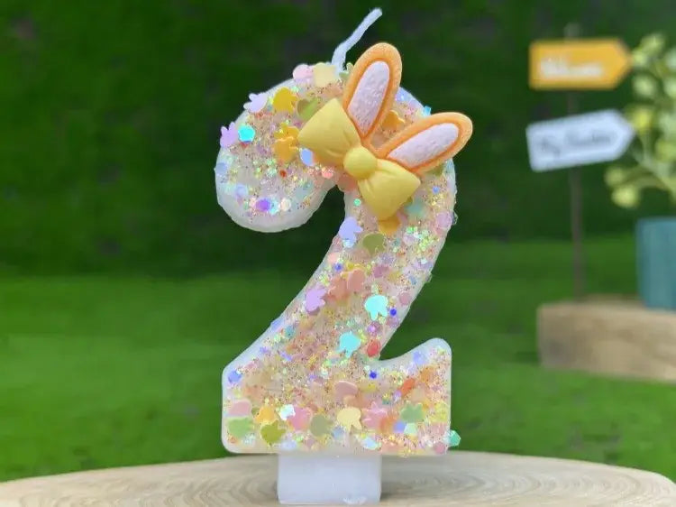 A translucent glitter-filled number two birthday candle adorned with a yellow and peach bunny ear bow.