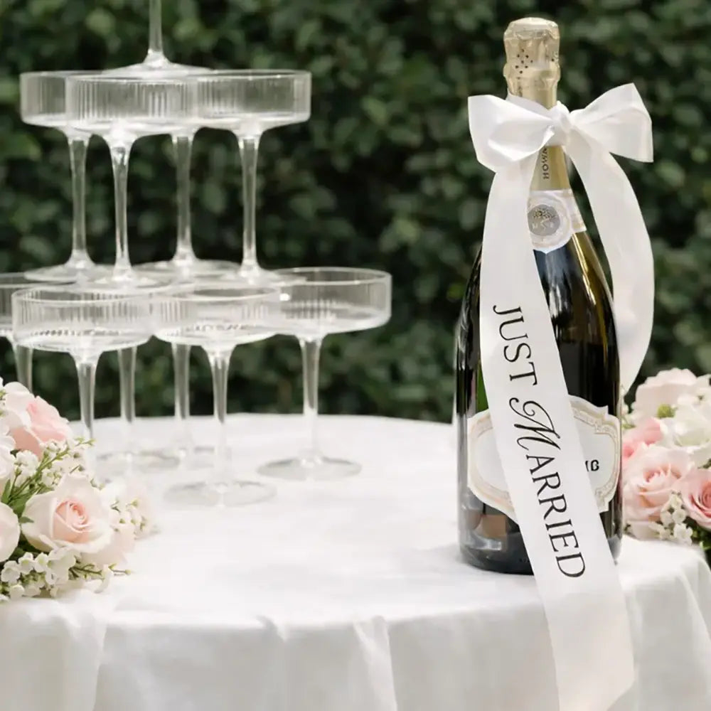 ダークグリーンのシャンパンボトルに、白いサテンのリボンで「just married」と読み取れる文字が描かれたものを蝶結びで首元に結び付け、結婚式の装飾用に仕上げています。