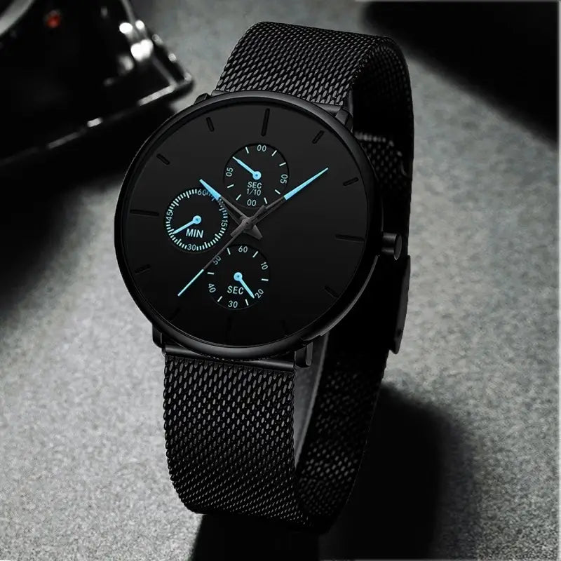 Montre à quartz à maille noire ultrafine pour hommes, avec un cadran noir minimaliste et des aiguilles bleu clair, ainsi qu’une sangle en maille noire.