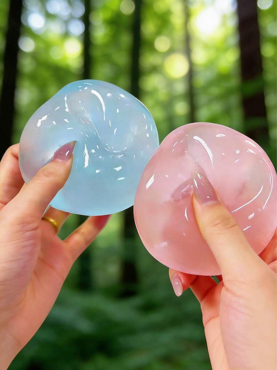 Deux balles anti-stress translucides de type gel, bleu clair et rose, tenues délicatement dans les mains, avec des ongles soignés, comme jouets de compression « Blue Coconut Oil Stress Ball ».