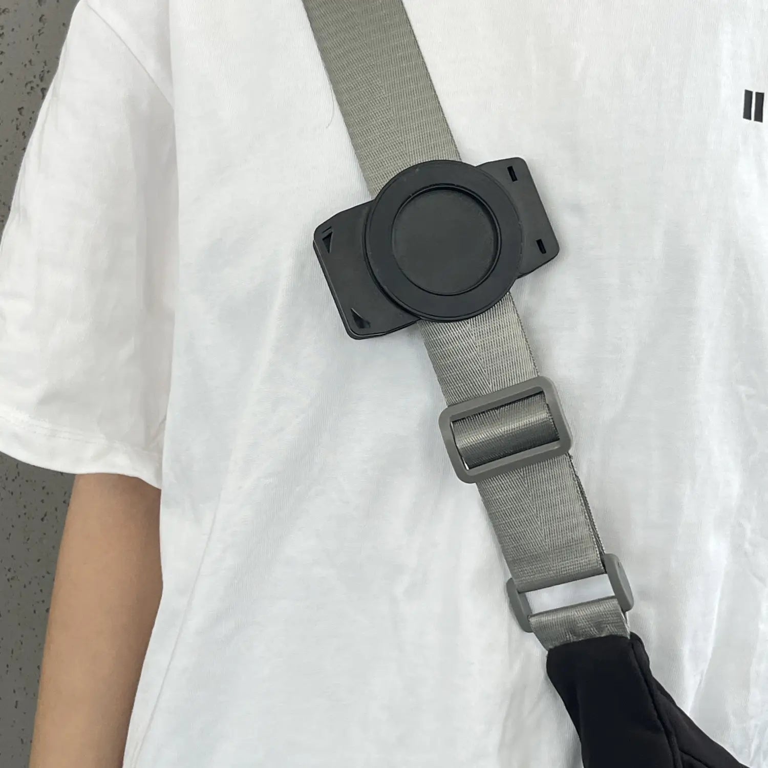 Grauer verstellbarer Riemen mit schwarzer Kunststoffschnalle und kreisförmigem Befestigungsstück auf der Rückseite einer magnetischen Telefon-Rucksackclip Universalhalterung.