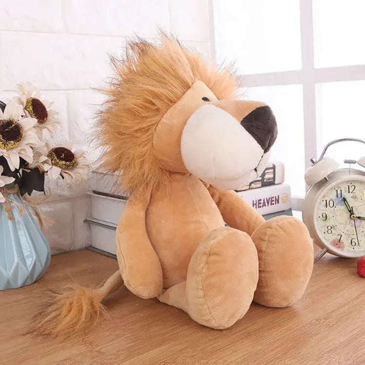 Un león de peluche color canela, animal de peluche relleno, con crin esponjosa y rasgos redondeados suaves, se encuentra sobre una superficie de madera en la colección de peluches de león, elefante y tigre.