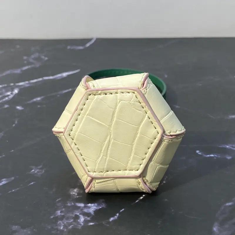 Un mini-sac hexagonal pâle jaune en cuir végétal gaufré façon crocodile et couture rose, utilisé comme charm de sac à main de créateur ou comme ornement de sac à main.