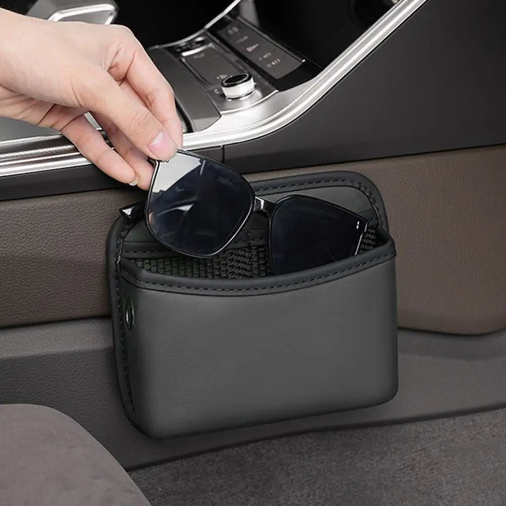 Pochette de rangement pour voiture en cuir synthétique noir avec adhésif, organisateur à intérieur en maille, contenant des lunettes de soleil pour une utilisation dans le véhicule.