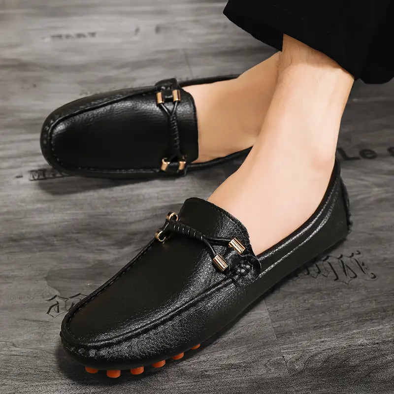 Les chaussures à enfiler habillées en cuir se portent sans effort avec des chaussures décontractées en cuir noir pour hommes, avec des boucles métalliques ton or et des semelles extérieures en caoutchouc orange.