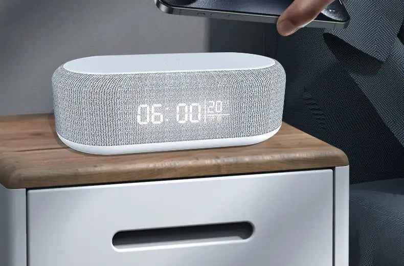 Haut-parleur Bluetooth en tissu gris avec affichage numérique blanc indiquant l’heure et la date, doté d’une fonction de charge sans fil et d’un mode d’économie d’énergie.