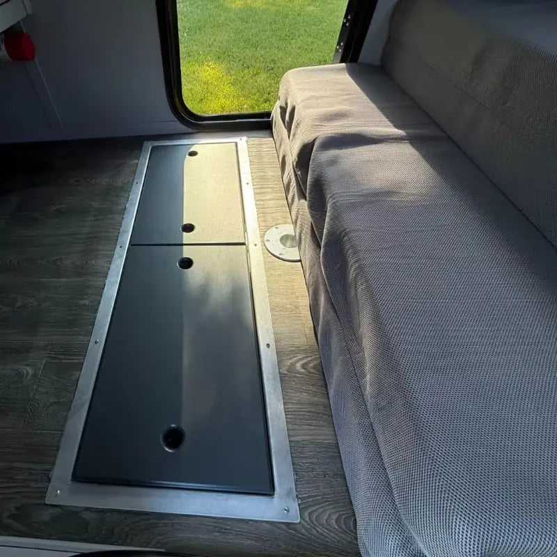 silver-framed black panel storage compartment with three circular cutouts and wood-grain floor in the back side of a custom teardrop travel trailer fully equipped camper