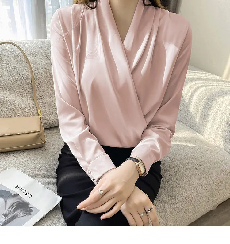 ドレープされたVネックラインと長袖を備えた、女性向けのやわらかなピンクサテンのブラウス。
