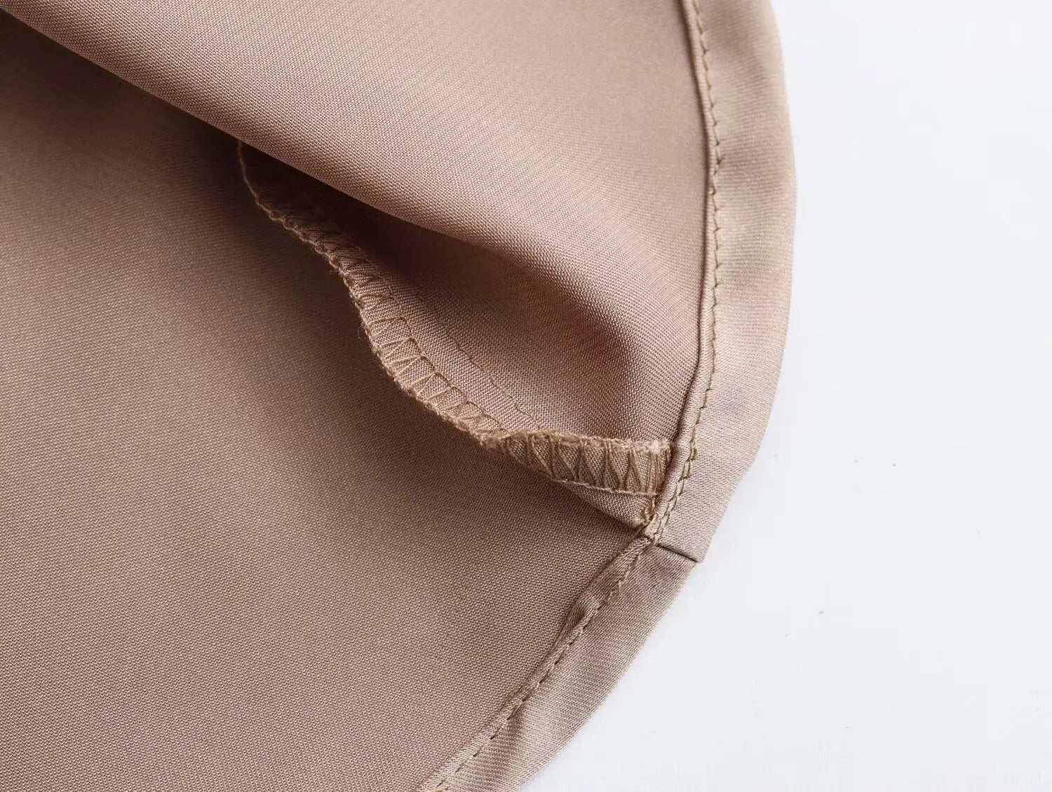 Jupe midi en satin beige, avec des points de couture assortis à l’identique le long de l’ourlet, à taille haute et design long élégant.