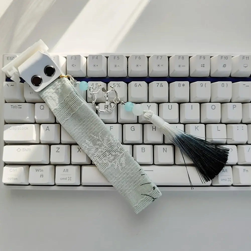 Sangle personnalisée délicate en dentelle gris clair pour le modèle Ribbon Dragon du clavier Wooting, avec un fermoir métallique à tons argentés, des perles turquoise et un pompon dégradé noir et blanc.
