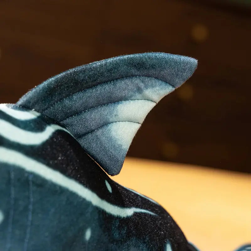 Plush hammerhead shark pillow soft toy showing the back side with dark gray and white striped fabric detailing on the tail.