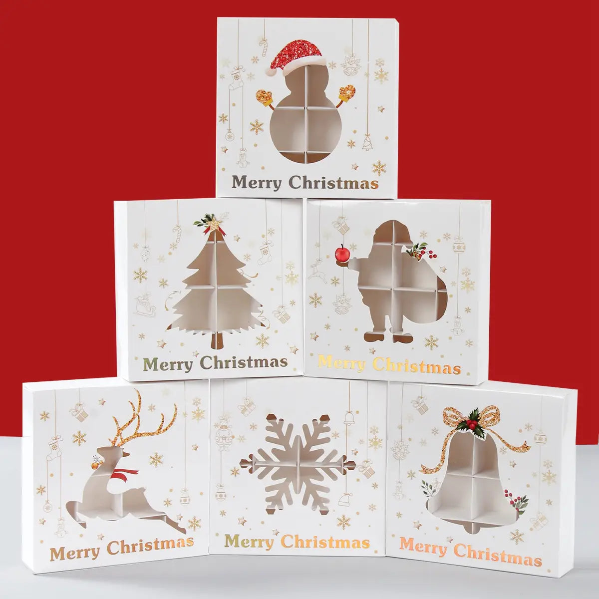 Christmas gift box paper treat packaging for cookies featuring white boxes with gold foil accents and cut-out designs of a snowman tree reindeer snowflake and bell.