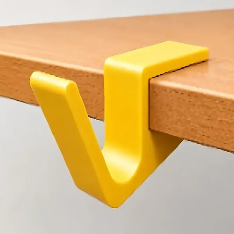 Bright yellow plastic desk edge bag hook with a v-shaped design for backpack holding.