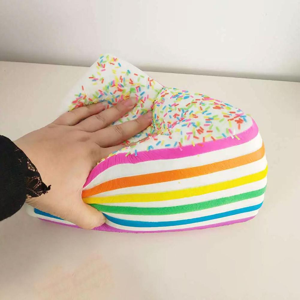Jouet antistress à gâteau arc-en-ciel à rebond lent, présentant un beignet souple, avec des rayures arc-en-ciel, un glaçage blanc et des vermicelles colorés.