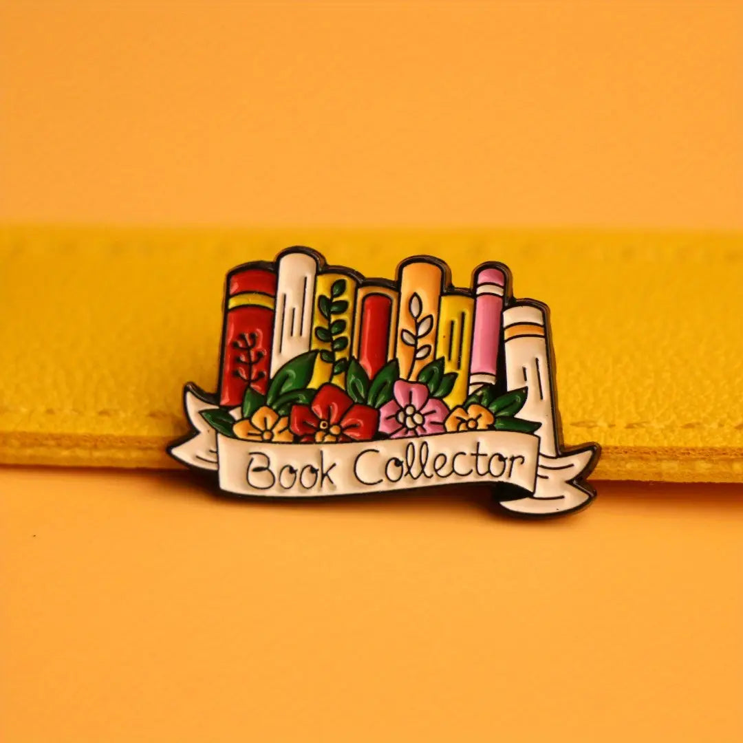 Une épingle émaillée colorée présentant une rangée de livres illustrés avec des touches florales et une bannière en forme de ruban portant l’inscription « book collector », conçue comme broche littéraire florale.