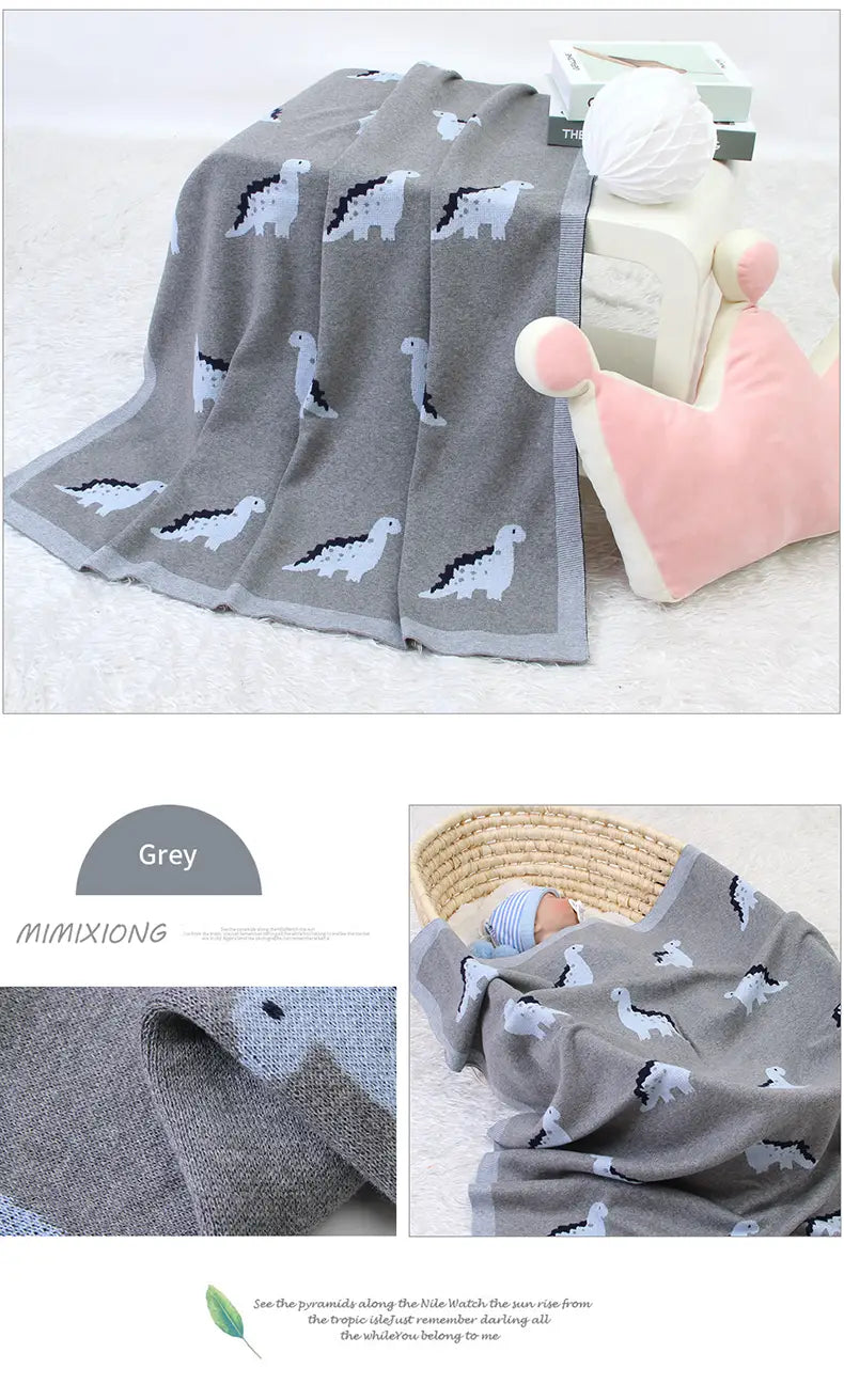 Graue gestrickte Baumwoll-Babyddecke mit weißen und schwarzen Dinosauriermustern und einer weichen, strukturierten Webart, entworfen als Wickeldecke für das Gitterbett.