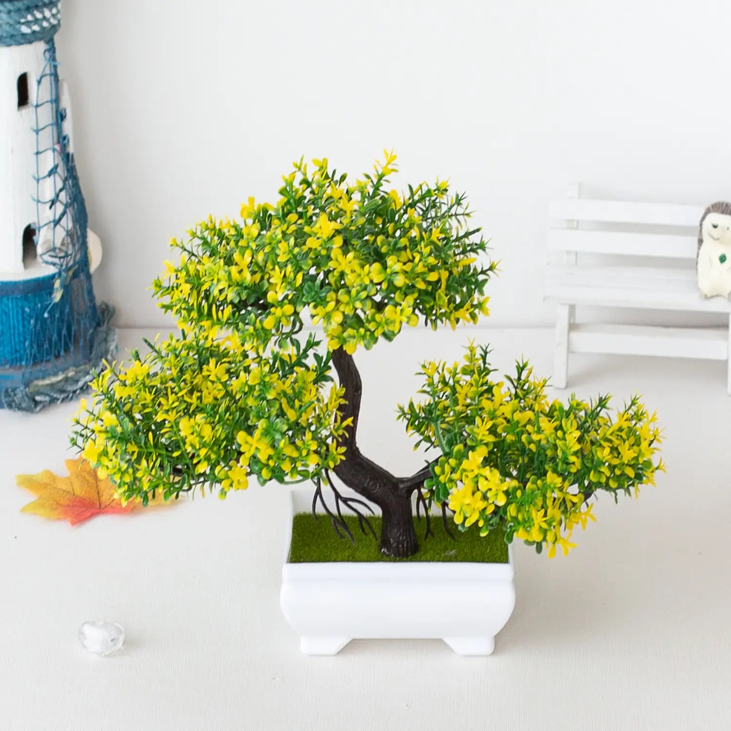 une plante artificielle de type bonsaï très vibrante jaune et verte, petit pot d’arbre, avec un tronc brun foncé planté dans un pot rectangulaire blanc, en contenant