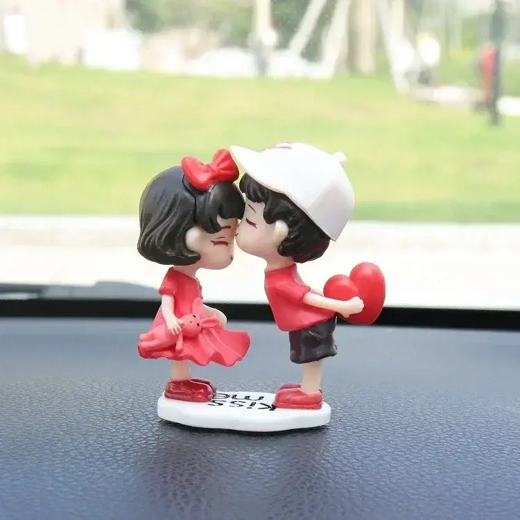 ハートを持つ白いキャップをかぶったキスしている男の子と、リボンの付いた赤いドレスを着た女の子をあしらった、魅力的な赤と白のレジン製カップルのカー・ダッシュボード用オーナメント。