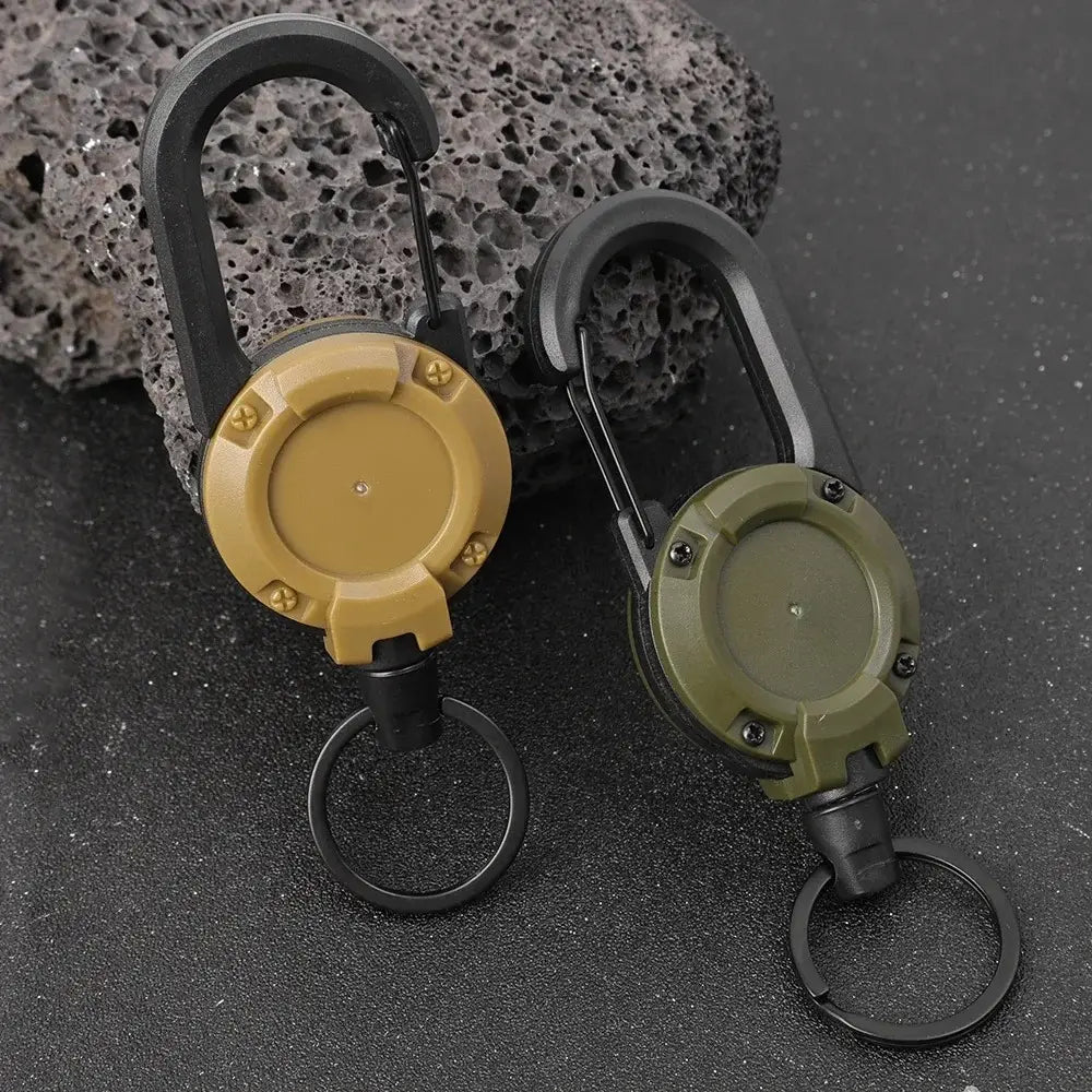 Two tactical-style retractable carabiner keychains in tan and olive green featuring heavy duty steel wire and black metal rings.