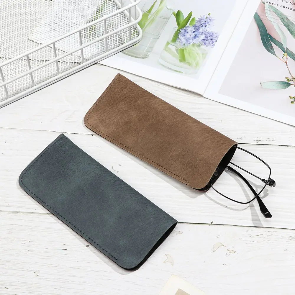 braune Wildleder- und dunkelgrüne Ledertaschen für Brillen mit abgesteppten Kanten und Reißverschluss, ausgelegt als Brillenzubehör, um ein Brillenpaar aufzunehmen.