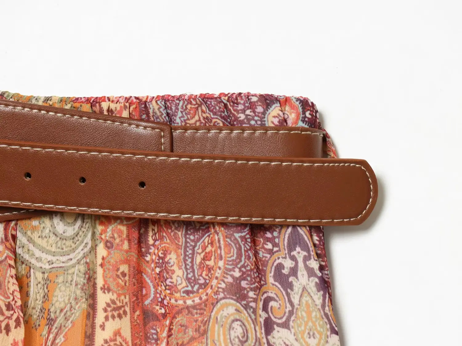 Ceinture marron en cuir avec surpiqûres apparentes, portée au-dessus de la ceinture de la jupe midi taille haute à imprimé cachemire.