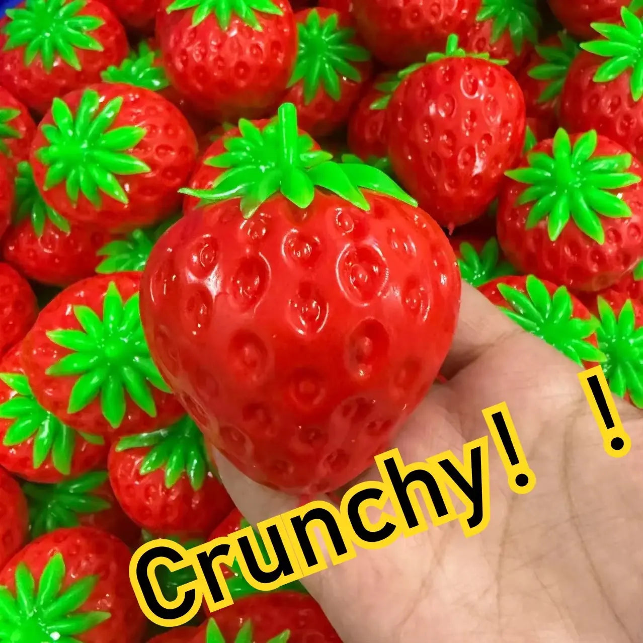 Une fraise en plastique brillant rouge vif, avec un dessus vert feuillu lumineux, conçue comme jouet à mâcher et à malaxer en forme de fromage pour soulager le stress et apaiser le stress lié au jouet.