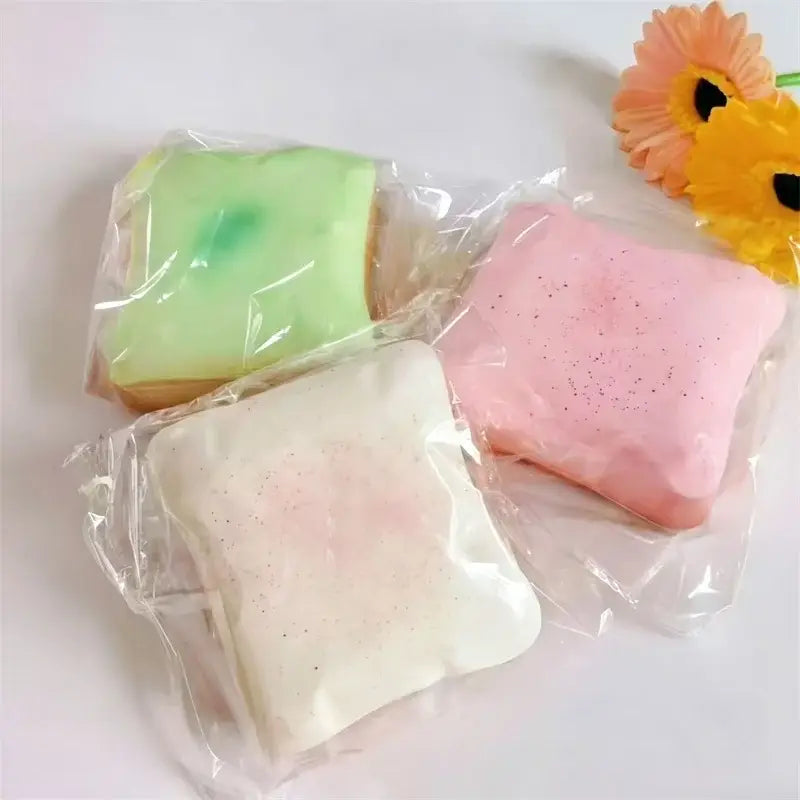 Trois jouets anti-stress en forme de toast moelleux de forme carrée, aux couleurs pastel, dans un emballage en plastique transparent, en couleurs macaron