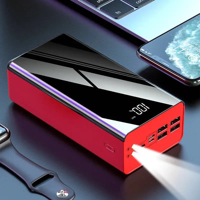 Rote und schwarze rechteckige Powerbank mit glänzender Oberfläche, mit mehreren USB-Anschlüssen und einer beleuchteten digitalen LED-Anzeige, die 100 Prozent Akkuladung anzeigt, kompatibel mit verschiedenen Ladegeräten und Modellen.