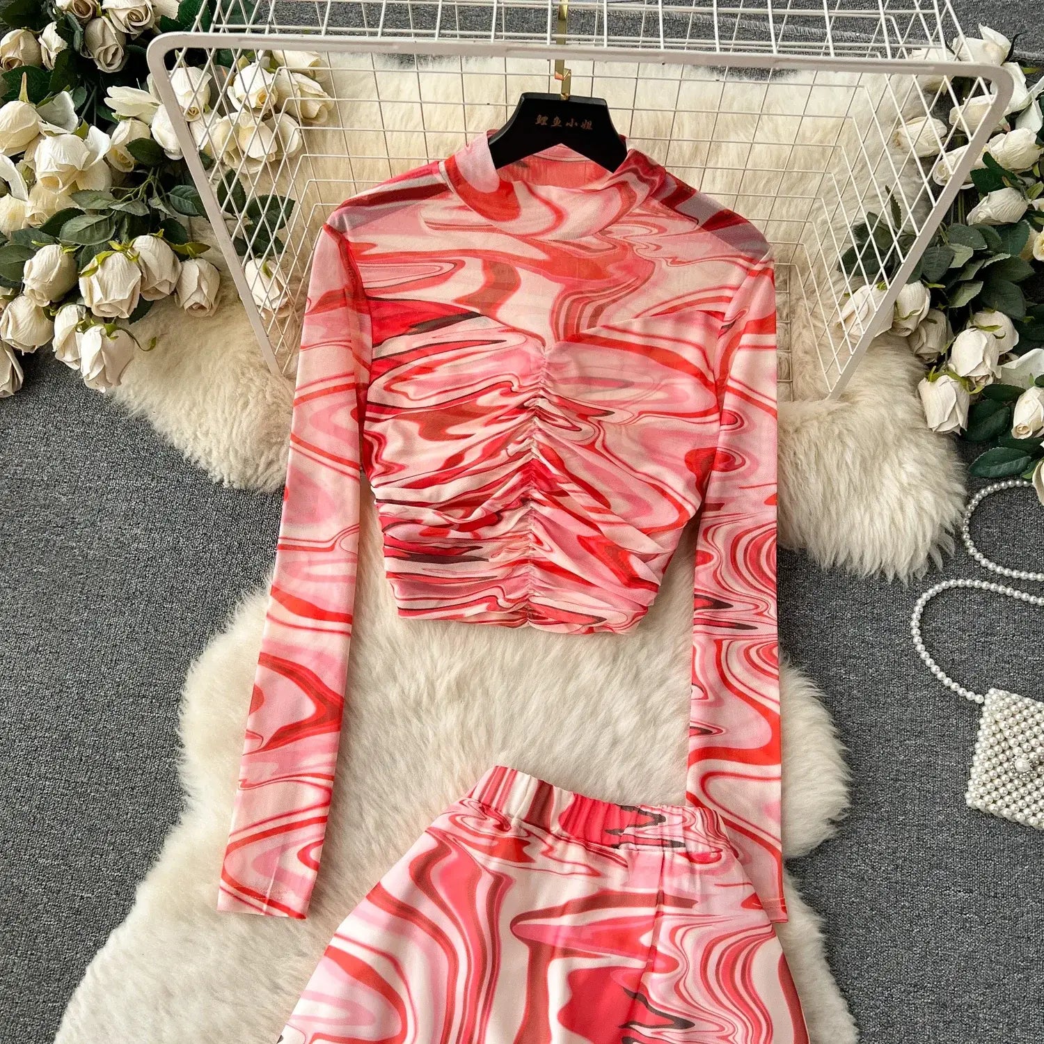 a two piece mesh skirt set featuring a long-sleeved high-neck top and coordinating pants with a vibrant pink and red marbled pattern on sheer mesh fabric with elastic closure type