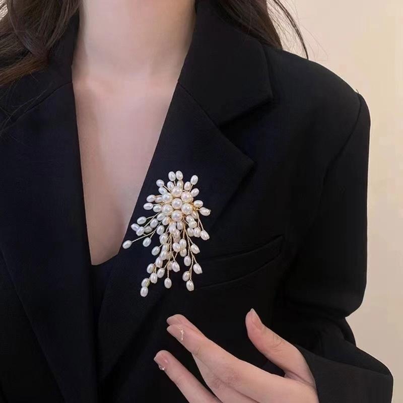 有機的なフローラルデザインに繊細なゴールドトーンの金属細工を施した、優雅な真珠の花のブローチピンであり、白真珠のカスケード状の連なりが特徴です。