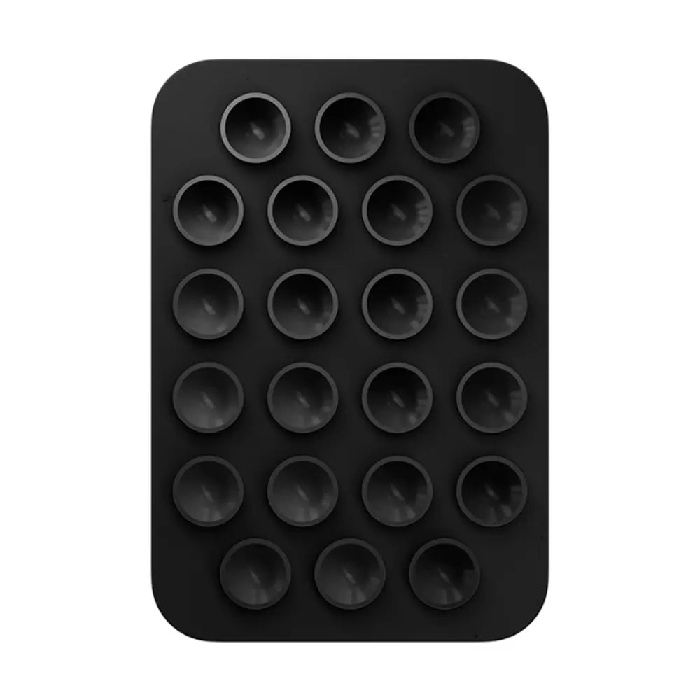 Un moule à cupcakes en silicone noir avec 24 cavités rondes peu profondes disposées en motif en grille, présenté avec un support de téléphone magnétique à ventouse pour iPhone Pro Max.