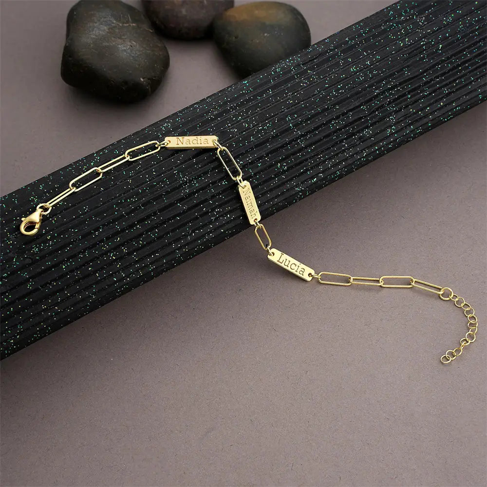Armband mit goldfarbenem Paperclip-artigem, individuell graviertem Lederarmband mit Namensanhänger für Herren mit gravierten Namensanhängern „nadia miguel“ und „lucia“.