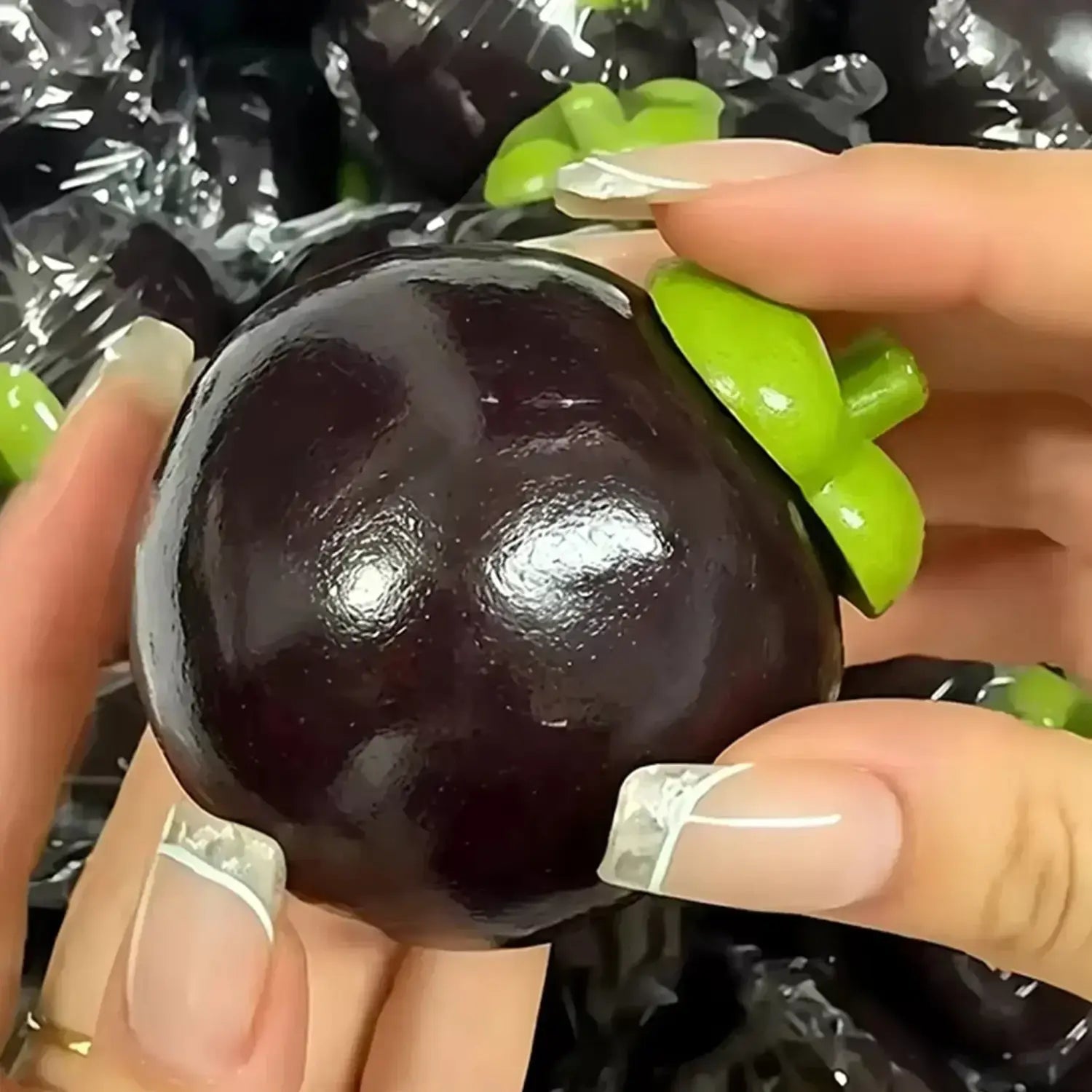 un jouet à mâcher et à malaxer en forme de fromage, mangoustan en plastique noir brillant, avec un dessus vert feuillu lumineux, conçu pour apaiser le stress lié au jouet et pour une utilisation de soulagement du stress