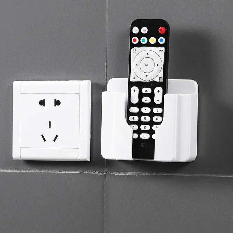 White plastic wall mount phone charging holder with integrated remote control holder holding a black tv remote with colorful buttons.