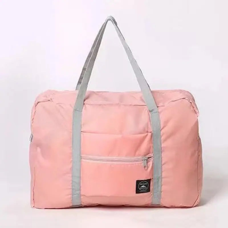 グレーのストラップと前面ジッパーポケットを備え、大型の女性用ラゲッジとして設計された、ピンクの折りたたみ可能なトラベルダッフルバッグ。
