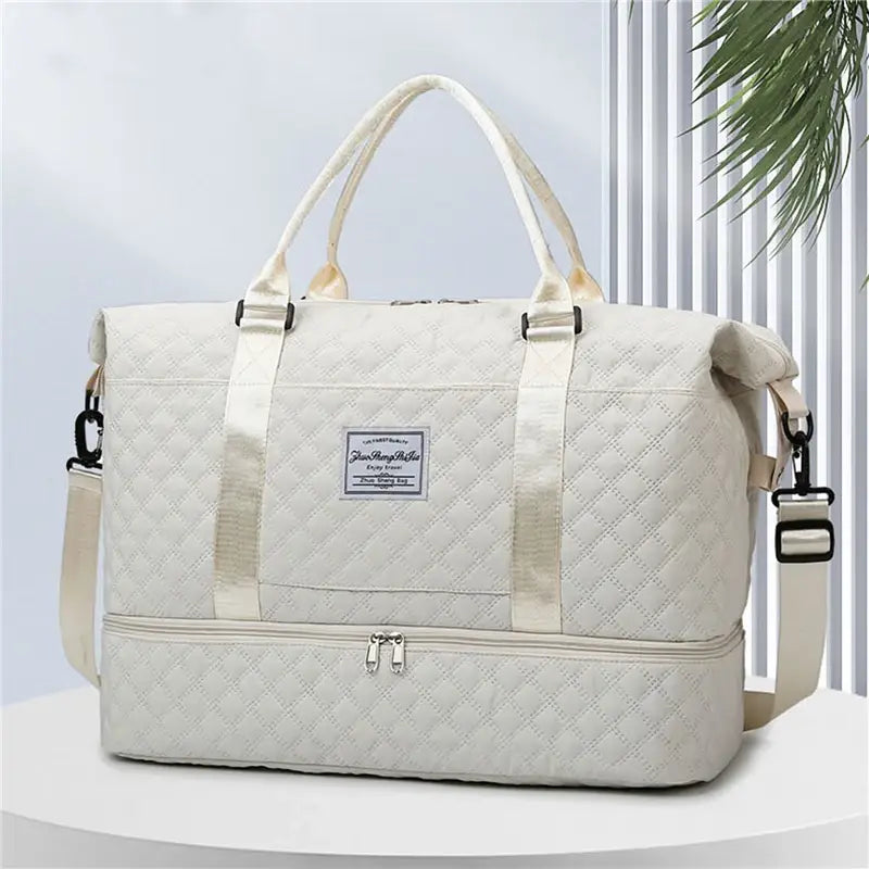 Bolsa de viaje tipo duffel acolchada de color crema, con correa ajustable para el hombro y asas superiores, diseñada como un tote weekender grande.