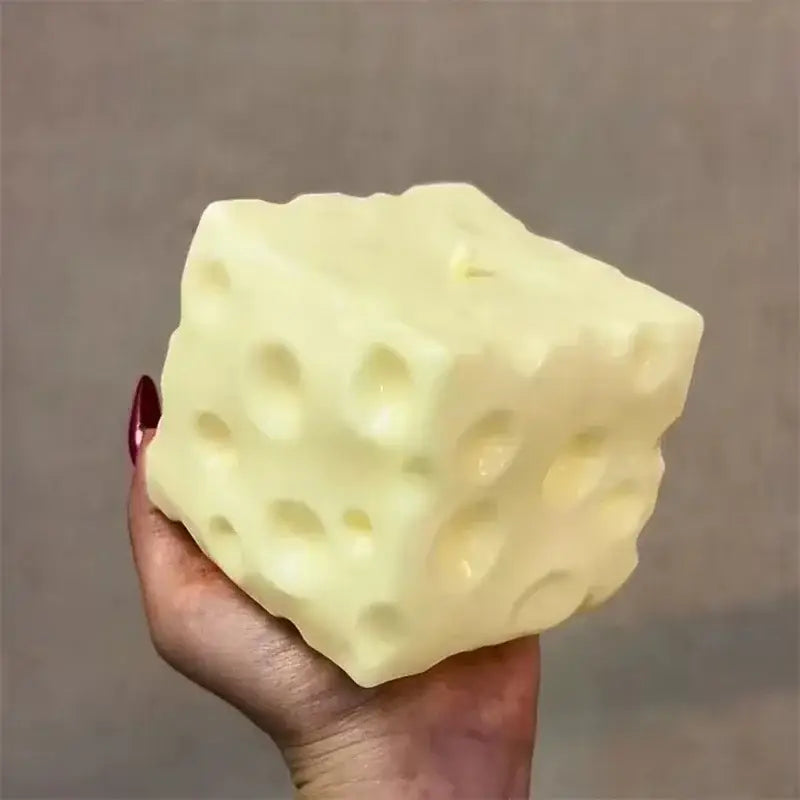 Un juguete antiestrés esponjoso con forma de cubo de queso amarillo, de color amarillo pálido, con una textura porosa y orificios espaciados uniformemente.
