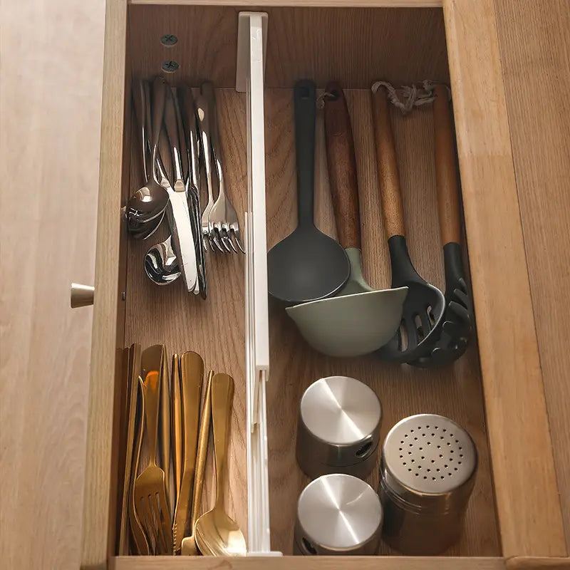 Tiroir de cuisine en bois bien organisé, comprenant un séparateur extensible d’organisateur de tiroir en plastique avec des ustensiles en acier inoxydable et dorés, des ustensiles de cuisson en silicone noir et vert, ainsi que des distributeurs métalliques.