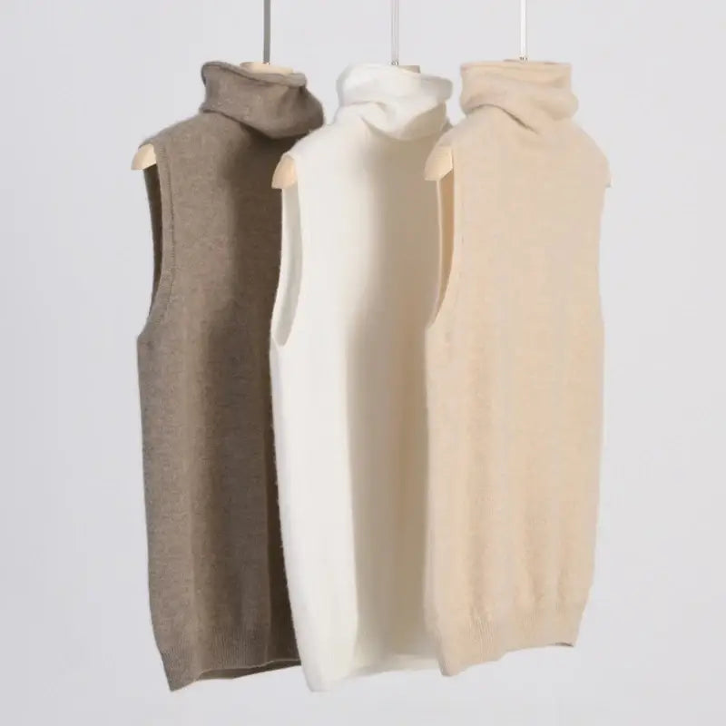 three sleeveless merino wool turtleneck vests for women in beige cream and taupe displayed on wooden hangers designed as slim knit base layers