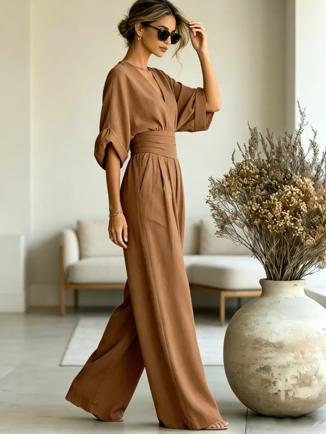 A flowing taupe v-neck wide-leg jumpsuit with a belted waist and soft fabric designed for elegant wear.