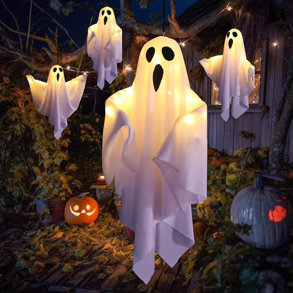A glowing white inflatable led hanging ghost halloween decoration with black eye and mouth cutouts suspended outdoors.