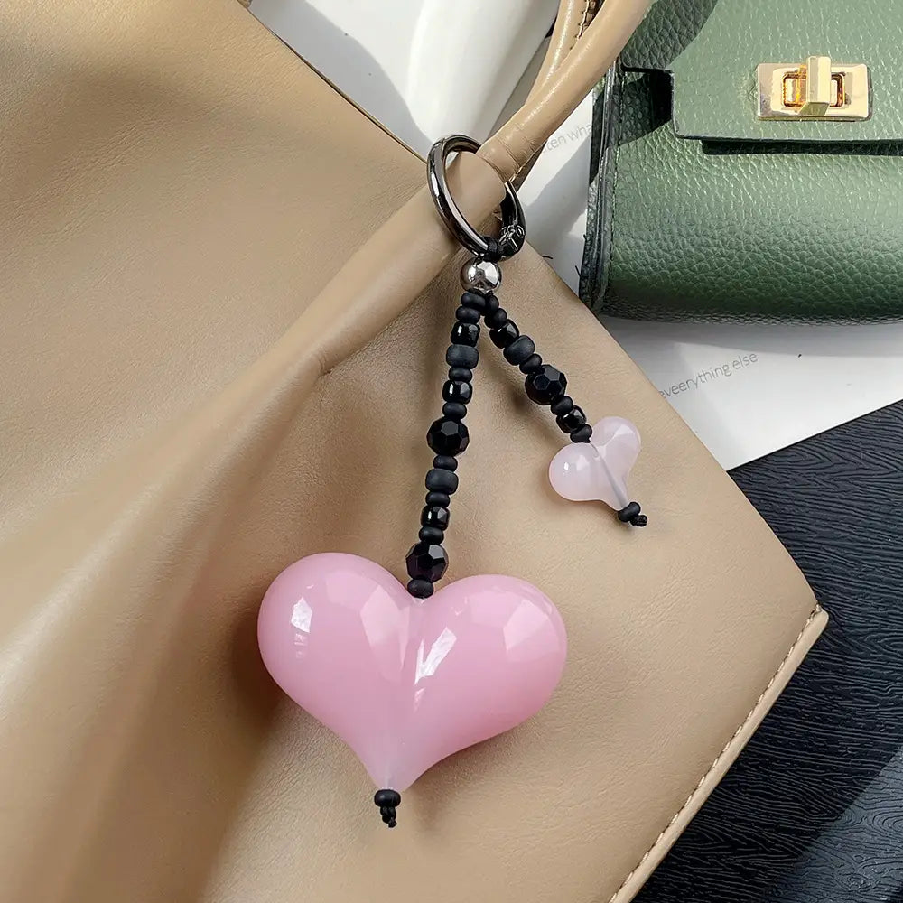 Pendentif pour sac à perles en forme de cœur, featuring un porte-clés en forme de cœur rose avec finition brillante, des perles noires et un petit pendentif en forme de cœur rose translucide.