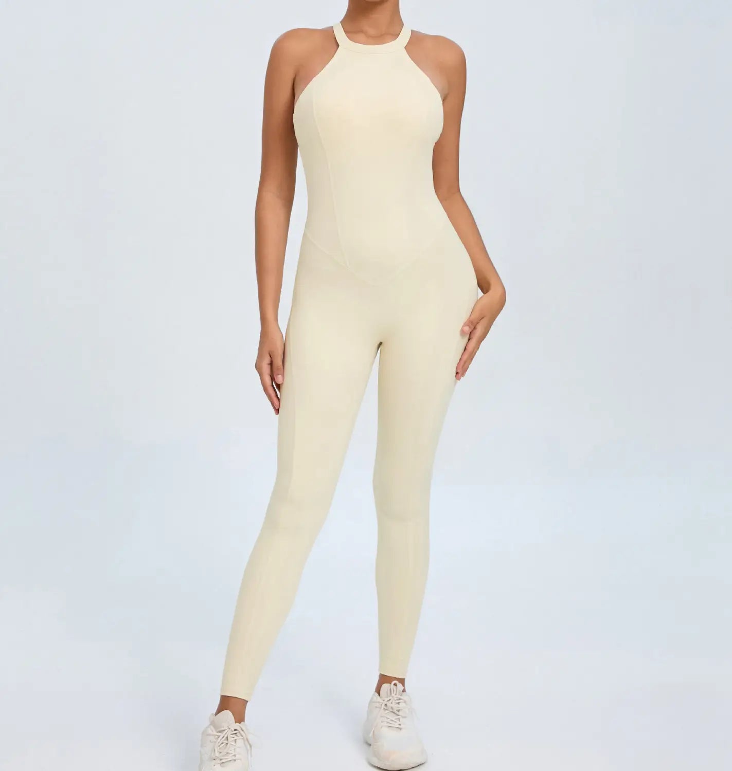 Cream-colored form-fitting one-piece athletic jumpsuit with a high neckline and halter straps designed for workout use.