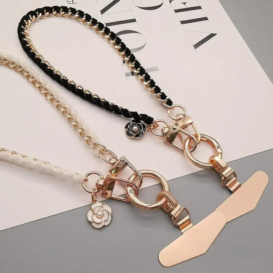 Handy-Handgelenkriemen aus goldfarbener Kette als Anti-Lost-Handylanyard, mit schwarzem und weißem geflochtenem Kord, goldfarbenen Metall-Verschlüssen und floralen Anhängern.