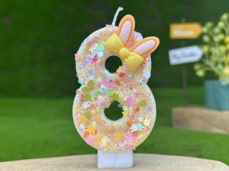 A glitter bunny ear number eight birthday candle in pastel colors decorated with a yellow bow and pink bunny ears.