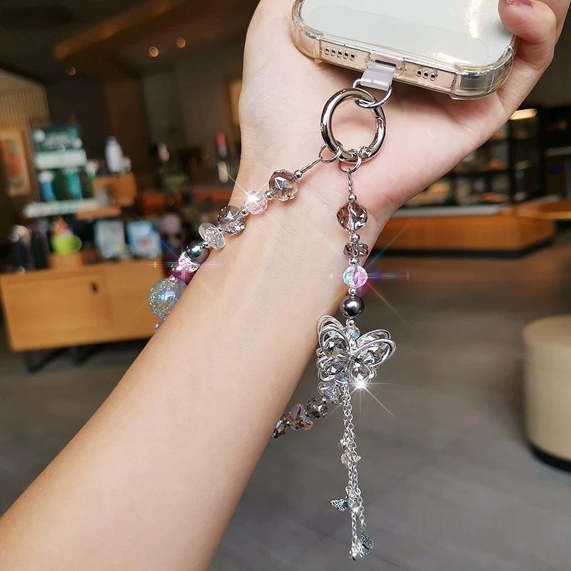 Un charme de chaîne pour téléphone à thème papillon argenté scintillant orné de perles en cristal transparent et rose, de sphères métalliques et d’une chaînette pendante pour un usage avec le téléphone mobile.