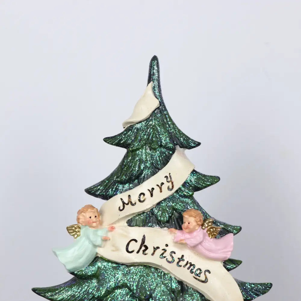 eine glitzernde Engel-Weihnachtsbaum-Harzfigurine mit einem glitzernden grünen Baum und zwei kleinen Engeln in Pastellkleidern, die ein weißes Banner halten, auf dem „Merry Christmas“ steht