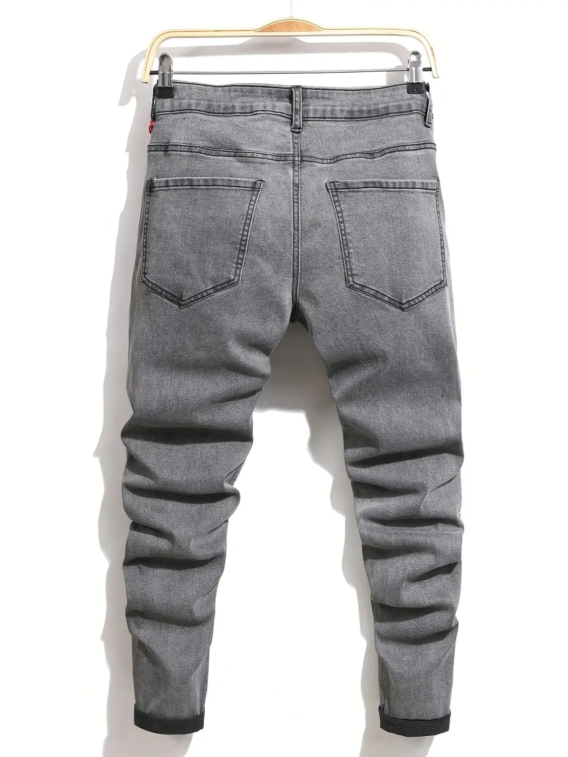 Herren-Ripped-Skinny-Bikerjeans grau, Slim-Fit-Denim, mit schwarzen Umschlägen und Ziernähten, die an einem Holzbügel hängen.